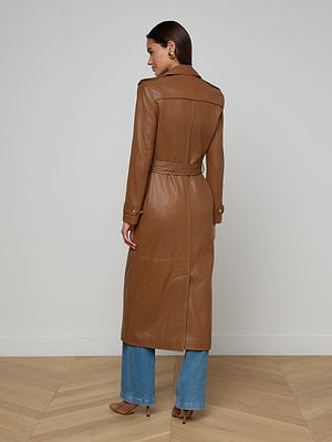 A woman stands indoors with her back to the camera, wearing the Baylee Leather Trench Coat, blue jeans, and brown heels on a light wood floor against a plain white wall.