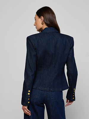 A woman with straight brown hair is seen from behind, wearing the L'AGENCE Emerson Blazer with gold sleeve buttons and matching denim pants against a plain light gray background.