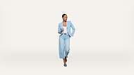 Woman in a light blue pantsuit and heels walking confidently against a plain white background.