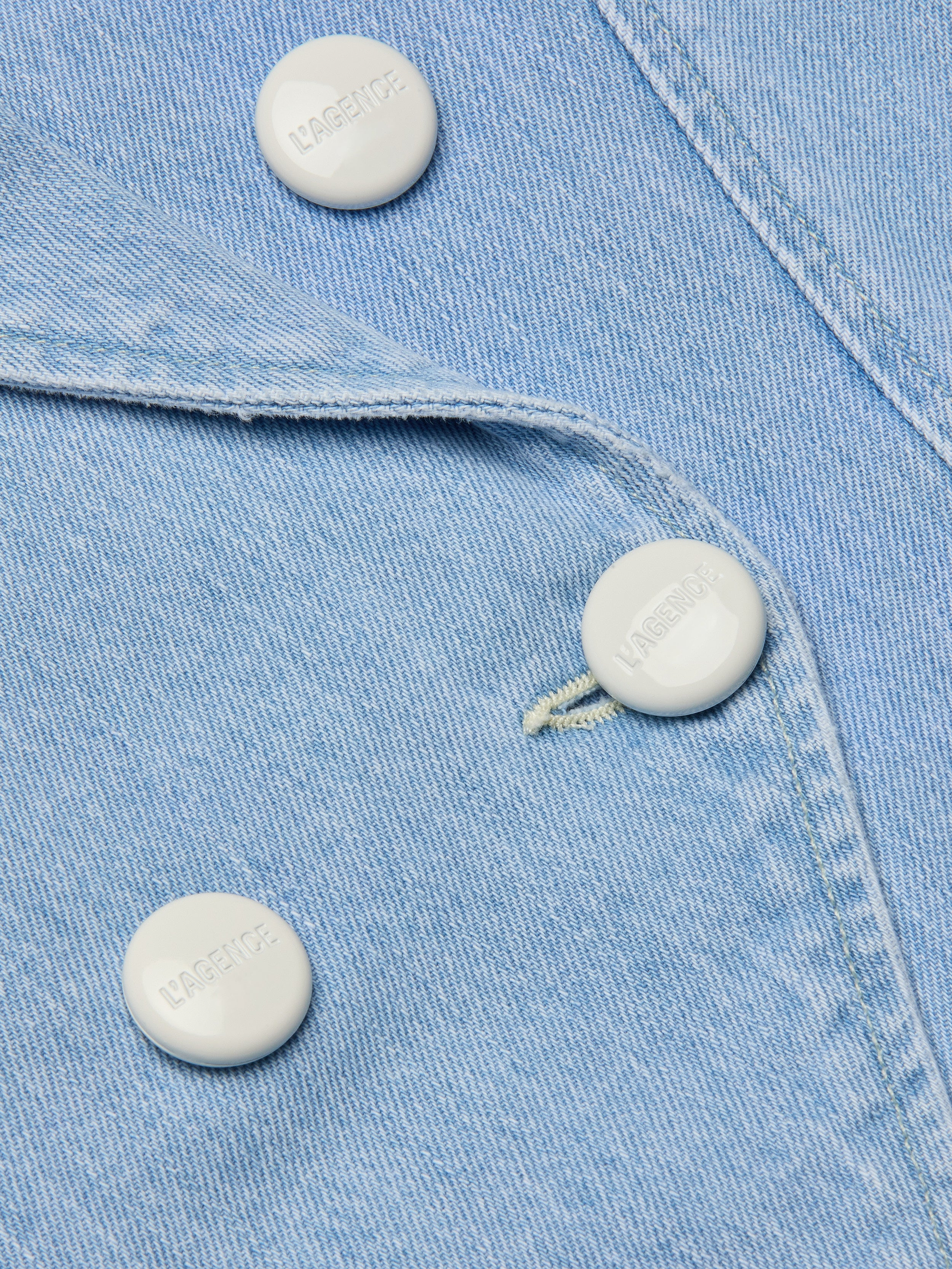 Close-up of the Emerson Structured Blazer in light wash, featuring all-cotton denim fabric with three visible white buttons and a buttonhole. The texture of the fabric and detailed stitching are clearly shown.