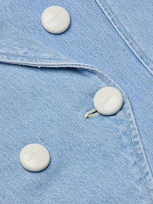 Close-up of the Emerson Structured Blazer in light blue denim, featuring a double-breasted front with three white buttons—two fastened, one open. The fine texture and precise stitching of the fabric are clearly shown.