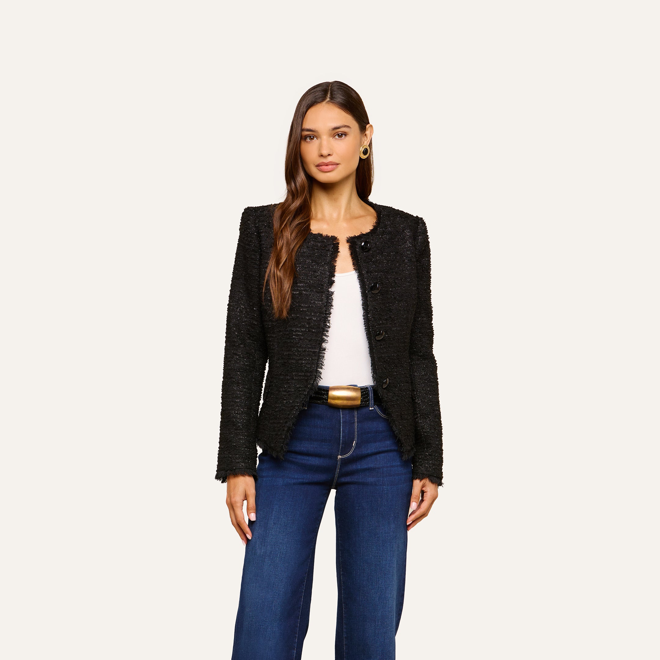 A woman wearing the Nerina Tweed Blazer over a white top and dark blue jeans stands against a plain light background.