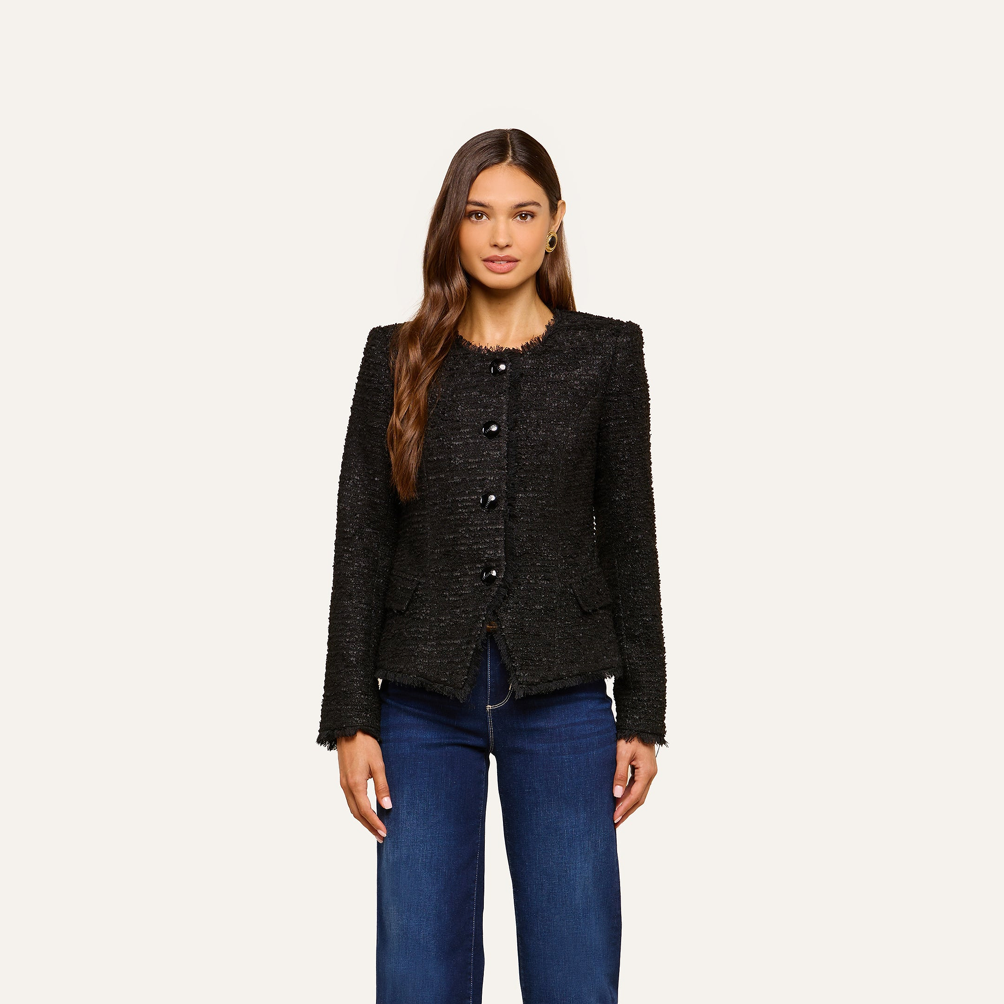A woman with long brown hair wears the Nerina Tweed Blazer over a white top and blue jeans, standing against a plain light background.
