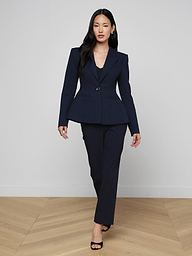 A woman in the Therese Blazer strides confidently in black heels against a plain white background.