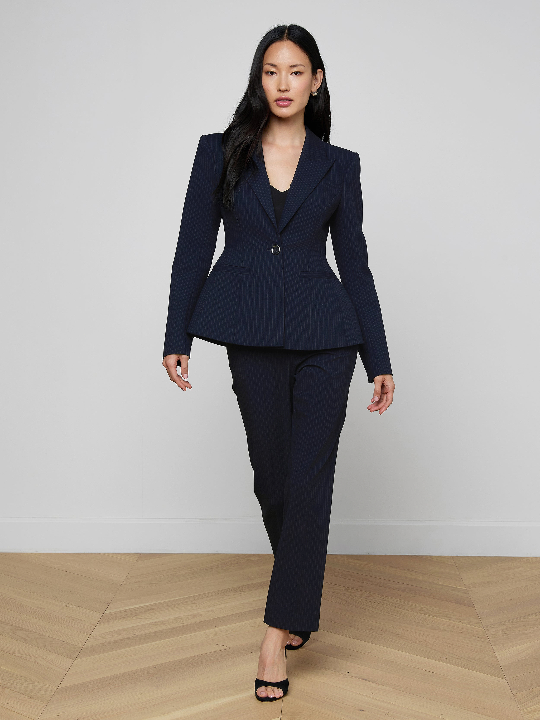 A woman in the Therese Blazer strides confidently in black heels against a plain white background.