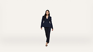 A woman in a dark suit and heels walks confidently toward the camera against a plain white background.