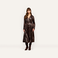 A woman wears an oversized, double-breasted Brinley Nylon Trench Coat in a dark, glossy finish, paired with dark brown heeled boots.