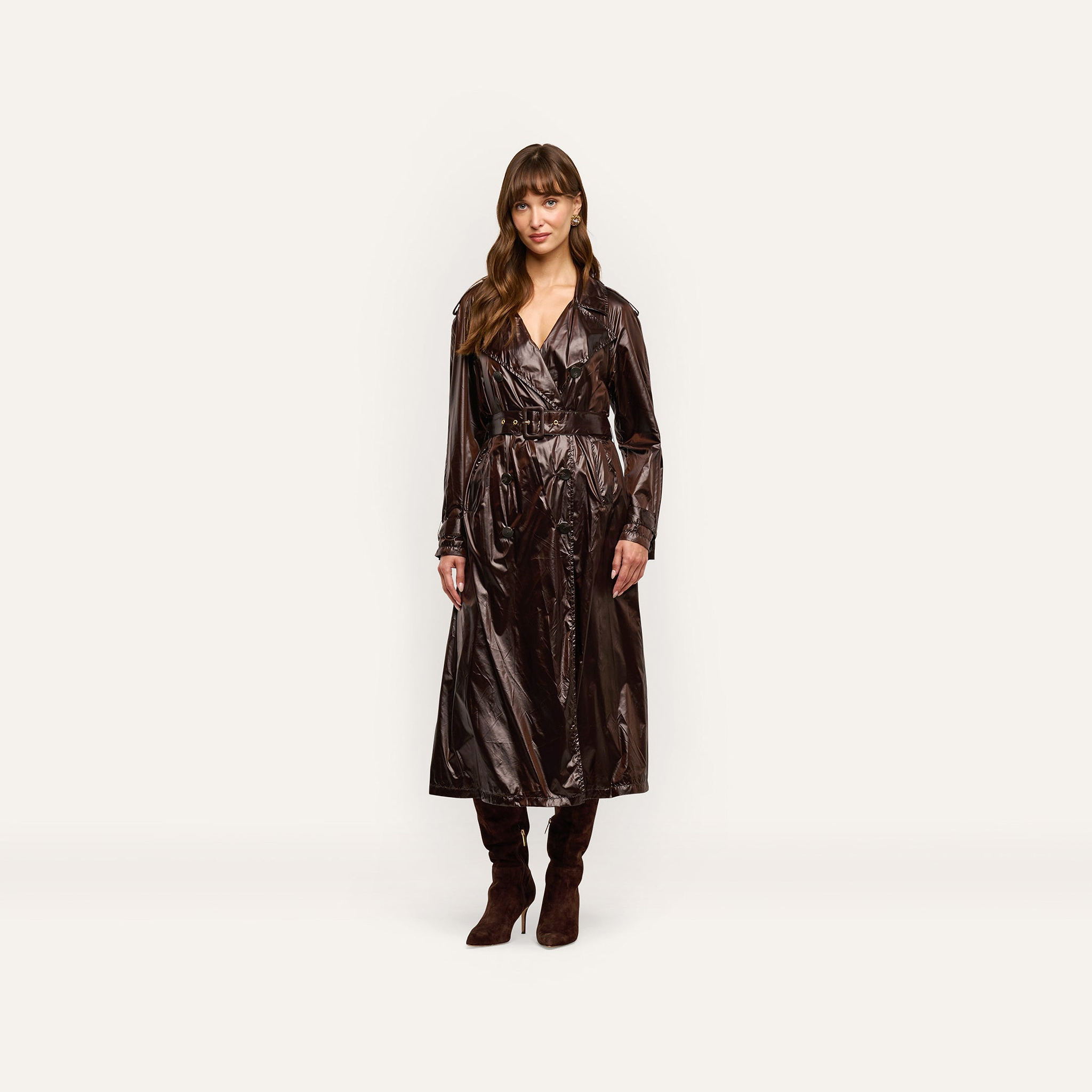 A woman wears an oversized, double-breasted Brinley Nylon Trench Coat in a dark, glossy finish, paired with dark brown heeled boots.