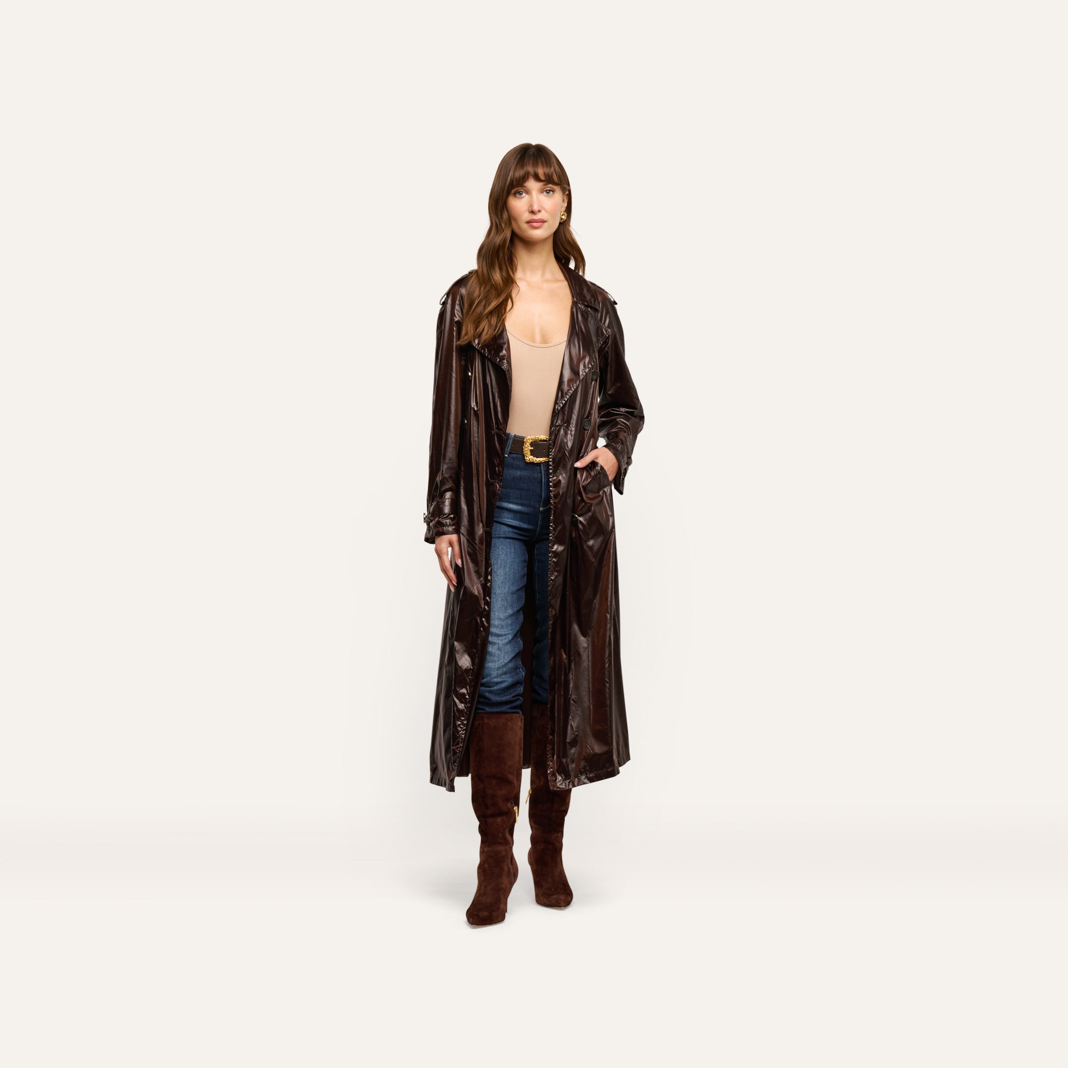 A person wearing a dark-brown Brinley Nylon Trench Coat over a beige bodysuit, blue jeans, and brown knee-high boots.