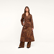 A woman stands against a plain background wearing the Brinley Oversized Trench Coat, a long belted leopard print style, paired with matching leopard print pants and black pointed shoes.