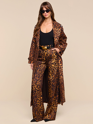 A woman wearing sunglasses and the Brinley Oversized Trench Coat from the latest women’s outerwear collection, paired with matching wide-leg pants and a black top, stands confidently against a plain beige background.