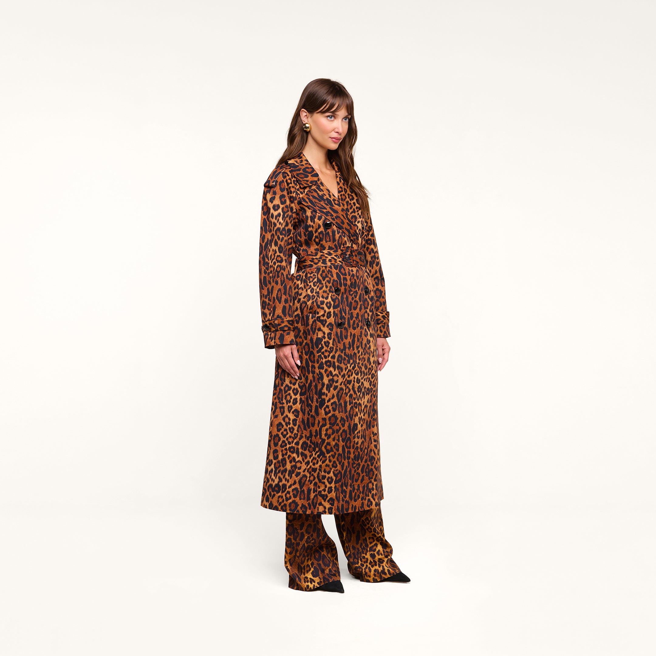 A woman stands against a plain background, wearing the Brinley Oversized Trench Coat in a leopard print with matching leopard-print pants and black pointed shoes.