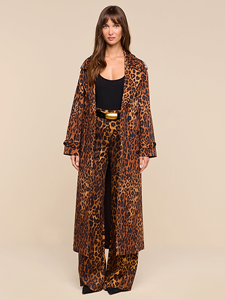 A woman stands facing forward, wearing the Brinley Oversized Trench Coat in a leopard print and matching wide-leg pants over a black top, cinched at the waist with a black and gold belt. The plain beige background accentuates this bold statement in women’s outerwear.