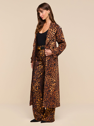 A woman stands against a plain beige background wearing the Brinley Oversized Trench Coat—a long, leopard-print statement piece—layered over matching wide-leg leopard-print pants and a black top for an effortlessly chic look.