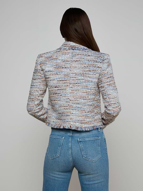 A woman with long brown hair, seen from the back, is wearing the Marv Tweed Blazer—a textured, multi-colored design with statement buttons—paired with high-waisted blue jeans against a plain light background.