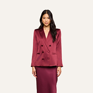 A woman with long black hair wears the Sena Silk Blazer in a shiny merlot red, paired with a matching skirt, standing against a plain light background.