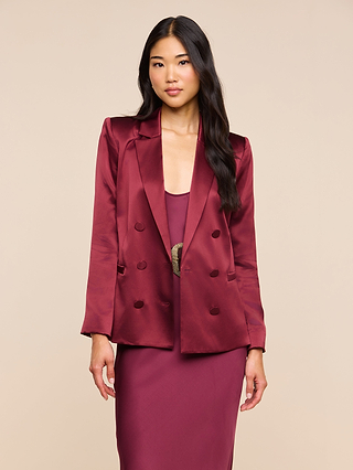 A woman with long black hair stands facing forward against a plain beige background, wearing the merlot red Sena Silk Blazer over a matching dress.