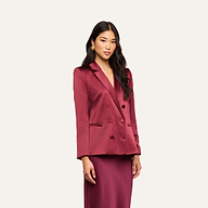 A woman with long dark hair wears the Sena Silk Blazer in merlot red, paired with a matching skirt, standing against a plain light background.