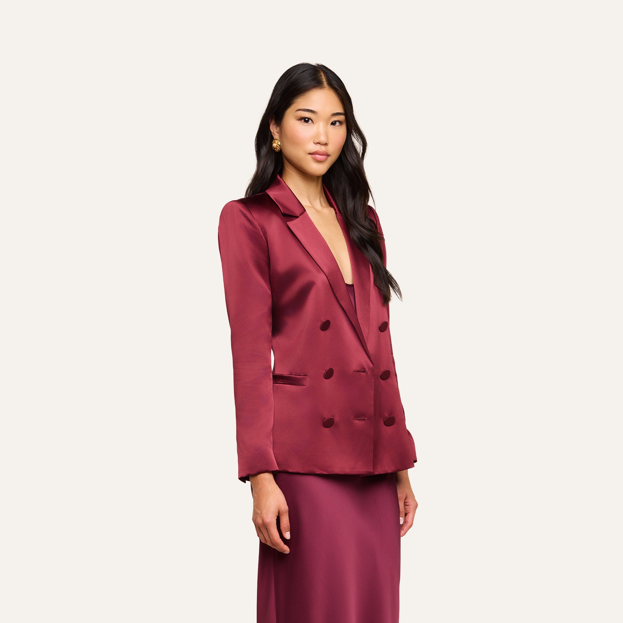 A woman wearing the Sena Silk Blazer in merlot red, paired with a matching skirt, stands against a plain white background and looks at the camera with a slight smile.
