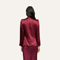 A woman with long dark hair, seen from behind, wears the Sena Silk Blazer in merlot red with a matching skirt, standing against a plain light background.