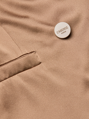 Close-up of the Sena Silk Blazer in beige, featuring a welt pocket and a round button embossed with LAGENCE PARIS. The smooth, slightly shiny silk charmeuse fabric emphasizes its elegant appeal.