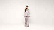 Woman standing against a plain white background, wearing a matching light-colored, floral-patterned blouse and wide-leg pants, with straight brown hair and a neutral expression.