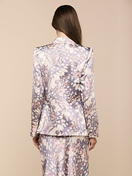 Von hinten sieht man eine Person mit langen braunen Haaren, die den Sena-Seidenblazer trägt - einen Zweireiher mit einem pastellfarbenen abstrakten Blumenmuster in Lila, Rosa und Weiß auf beigefarbenem Hintergrund.