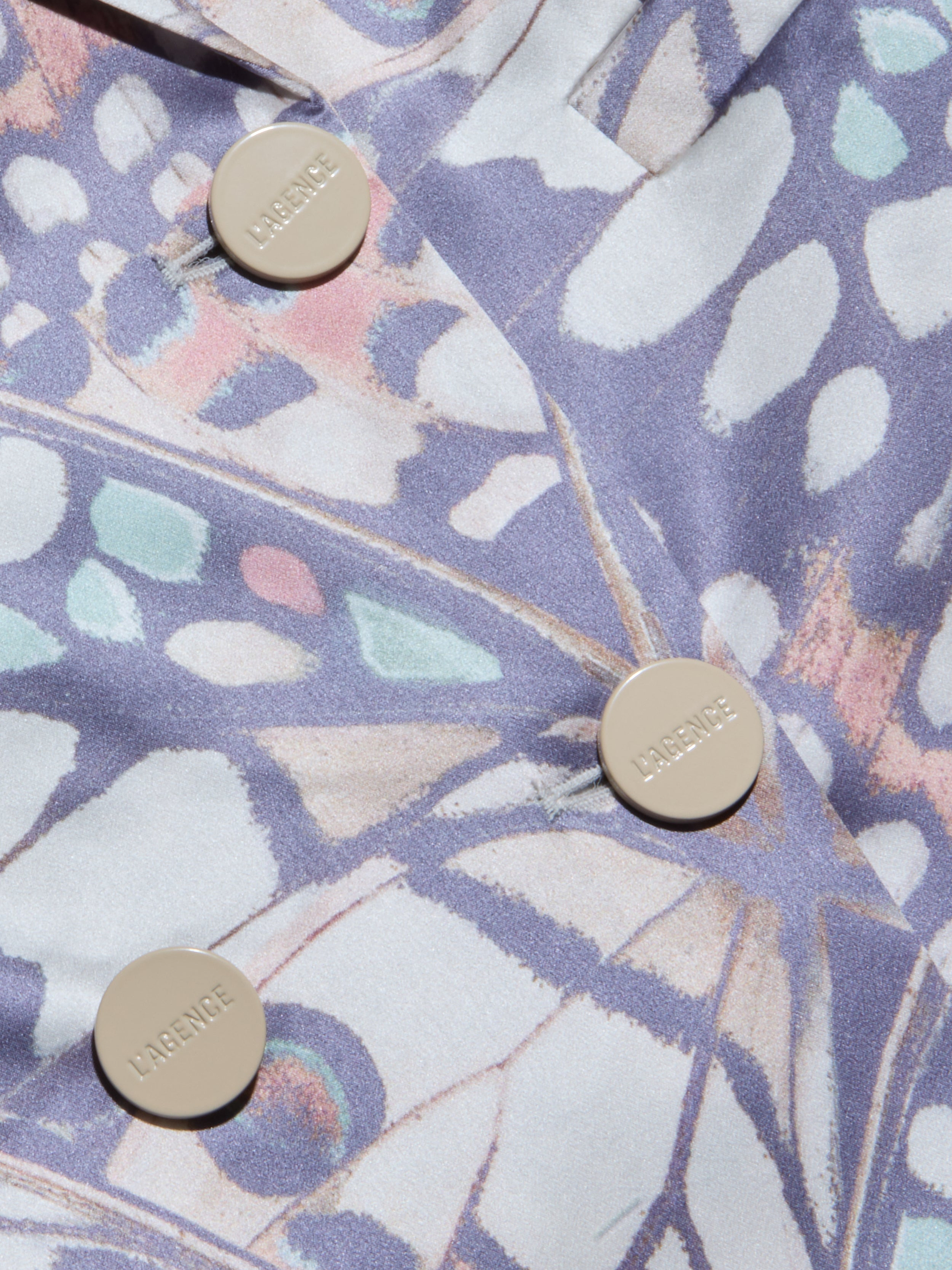 Nahaufnahme des Sena Silk Blazers, eines pastellfarbenen Zweireihers mit drei beigen LARENCE-Knöpfen. Das abstrakte Muster mischt zartes Blau, Rosa und Lavendel in organischen, blattähnlichen Formen, die von Schmetterlingsflügeln inspiriert sind.