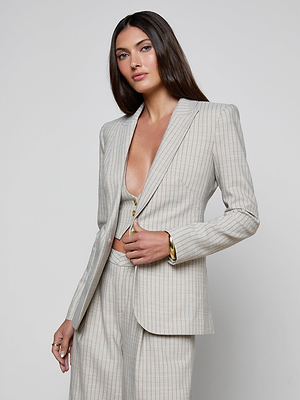 A woman with long, straight brown hair models the Sheila Longline Blazer, a light-colored pinstripe suit with a deep neckline and gold jewelry, standing against a plain white background.