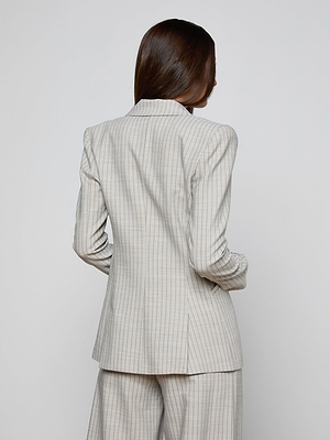 A person with long brown hair is standing with their back to the camera, wearing the Sheila Longline Blazer and matching pants in a light-colored, Italian wool-blend plaid pattern.