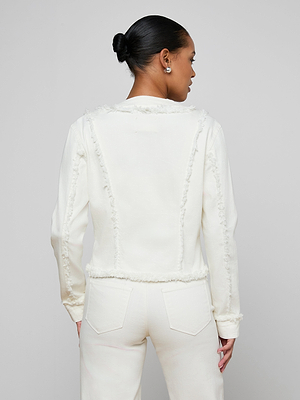 Someone with their hair in a neat bun models the Yarin Collarless Fray Jacket, a white textured blazer, with matching pants, viewed from the back against a plain light gray background.