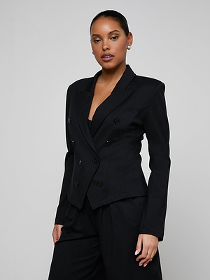A person stands confidently against a plain background, wearing the Emerson Ponte Blazer—a tailored black double-breasted jacket with a sculpted silhouette—and matching black pants, hair pulled back and a neutral expression.