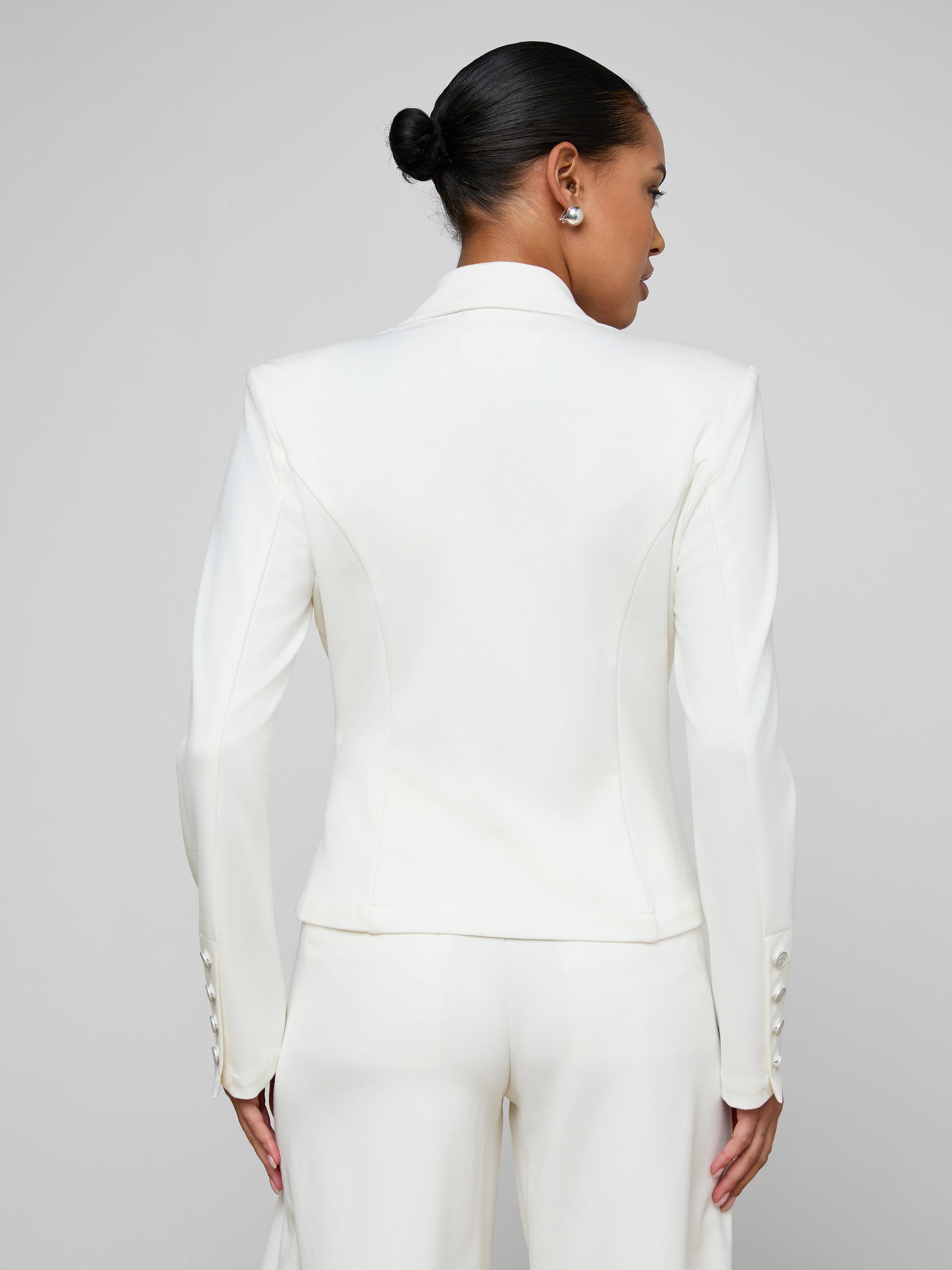 A woman with her hair in a bun models the Emerson Ponte Blazer, a white double-breasted suit jacket, shown from the back against a plain light background.