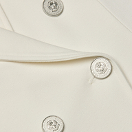 Close-up of the Emerson Ponte Blazer in white, showcasing shiny silver buttons with an embossed emblem. The smooth fabric and a portion of the lapel are visible.