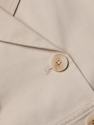 Close-up of the Novelle Lace Trench in beige, highlighting the lapel, light tan button, and buttonhole detail on the smooth fabric—a perfect lightweight layer for effortless style.