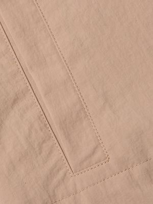 Close-up of light beige nylon on the Calida Windbreaker Trench reveals a rectangular stitched seam—possibly a pocket or decorative detail—with visible stitching lines on the smooth, water-repellent fabric, ideal for this stylish trench coat.