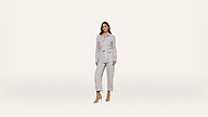 A woman wearing a light gray belted jacket and matching pants stands against a plain white background, posing in high-heeled sandals.