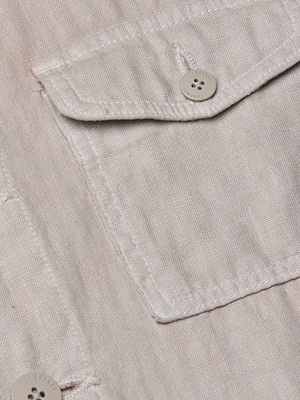 Close-up of the Samaya Linen Jacket in light pink or beige, highlighting a buttoned chest pocket with visible stitching, detailed fabric texture, and a four-hole button—evoking classic utility jacket features.
