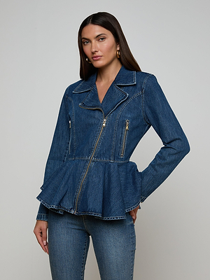 A woman wears the Moxie Peplum Biker Jacket, a blue denim design with a peplum silhouette, front zipper, and zippered pockets, paired with matching denim pants against a light gray background.