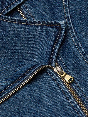Close-up of the Moxie Peplum Biker Jacket in blue denim, featuring a partially unzipped gold zipper, detailed stitching, and rich fabric texture.