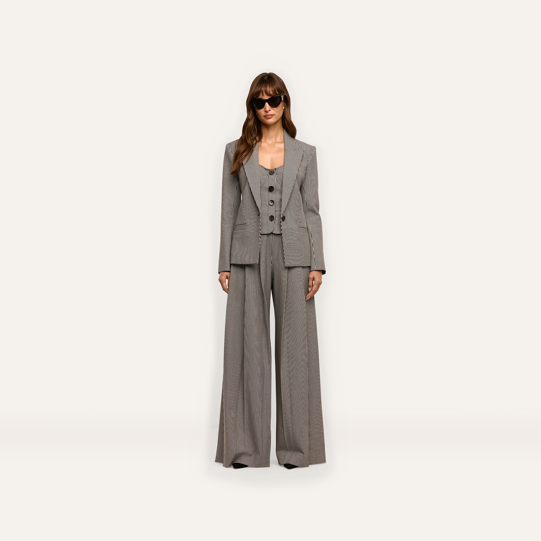 A person wearing a Blanche Blazer in a fitted houndstooth pattern, styled with a button-up vest, matching wide-leg trousers, and sunglasses.