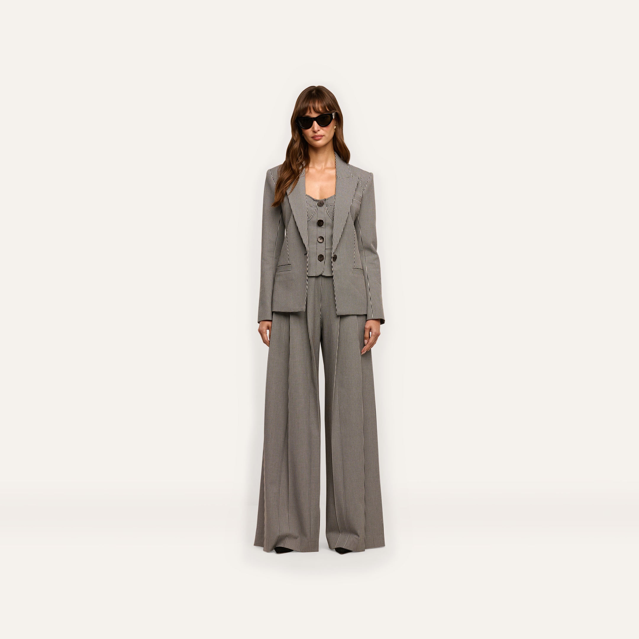 A person wearing a Blanche Blazer in a fitted houndstooth pattern, styled with a button-up vest, matching wide-leg trousers, and sunglasses.