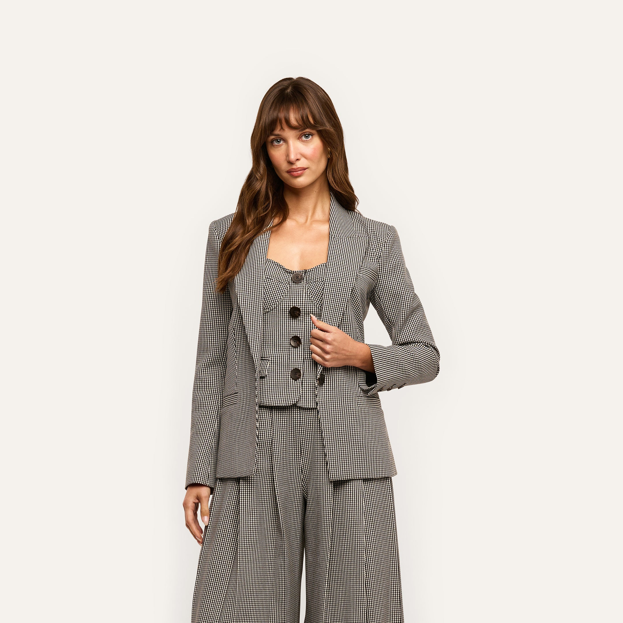 A person wearing a black and white houndstooth Blanche Blazer over a matching button-up vest and wide-leg trousers.