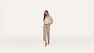 A woman stands against a white background, wearing a beige short-sleeve jacket, matching wide-leg pants, a white top, and beige heels.