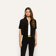 A woman wears a black velvet Kirstie Velvet Shirt Jacket over a white top and black pants.