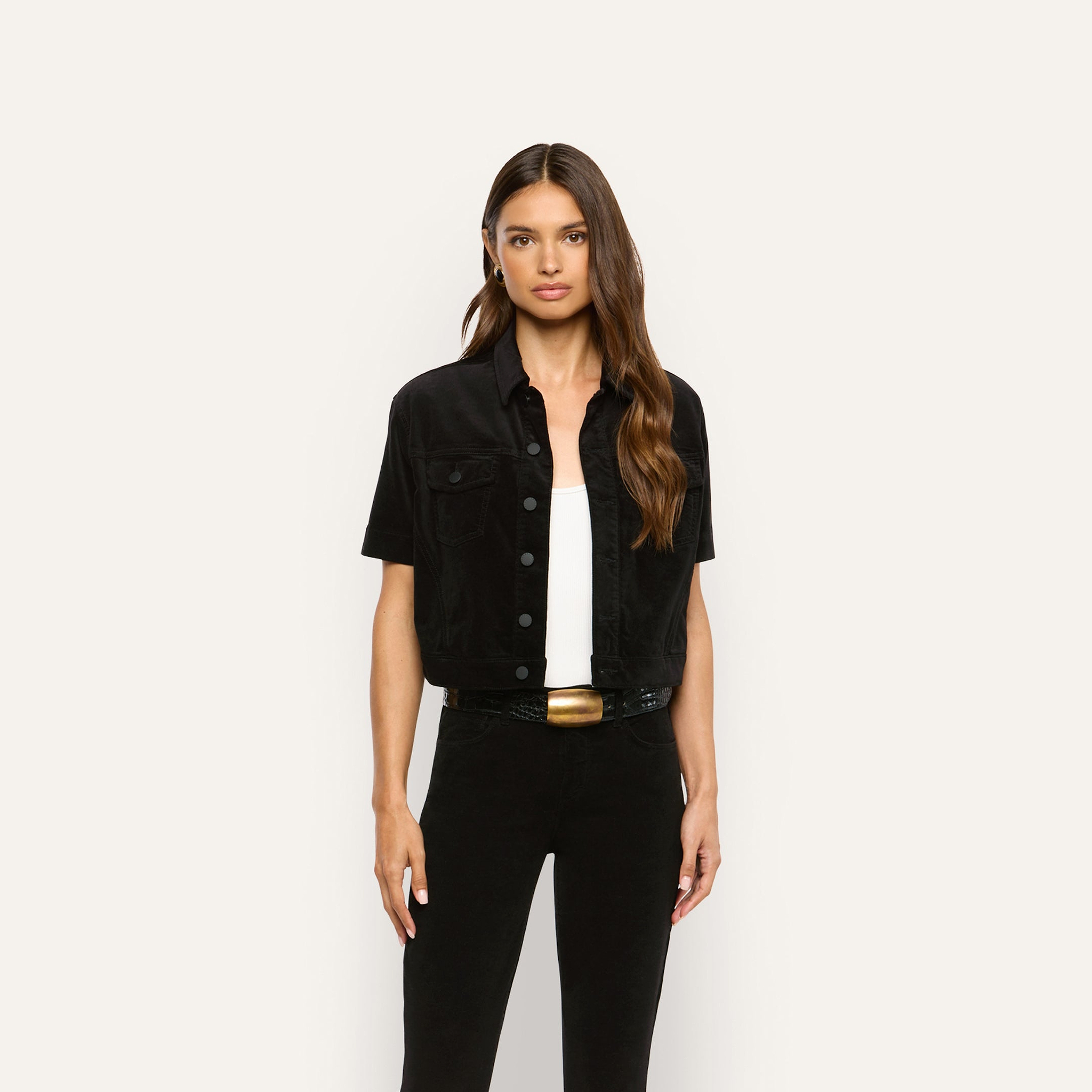 A woman wears a black velvet Kirstie Velvet Shirt Jacket over a white top and black pants.