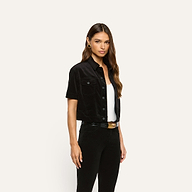 A woman wears a black velvet Kirstie Velvet Shirt Jacket over a white top and black pants.