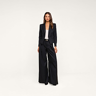 A woman stands facing forward against a plain beige background, wearing the Misa Blazer paired with wide-leg trousers, a white top, and black heels.