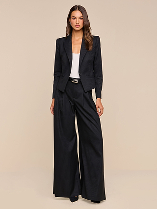 A woman stands facing forward against a plain beige background, wearing the Misa Blazer paired with wide-leg trousers, a white top, and black heels.