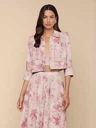 Woman wearing the Eda Cropped Linen Jacket in light pink with a red botanical and tropical print, paired with a matching high-waisted skirt, standing against a beige background.